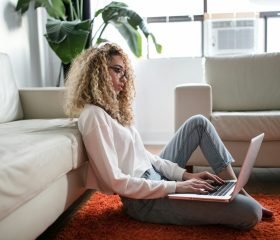 woman sitting on floor and leaning on couch using laptop