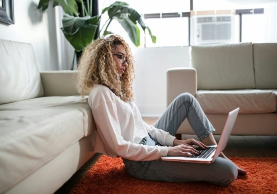 woman sitting on floor and leaning on couch using laptop